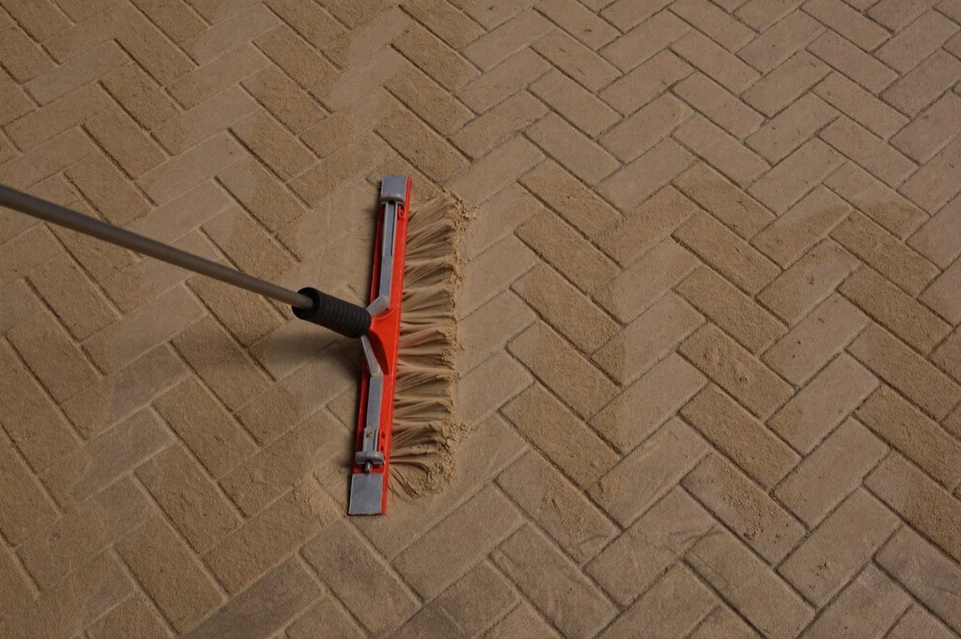 Sweeping polymeric sand into herringbone paver joints — the laying pattern changes the waste factor