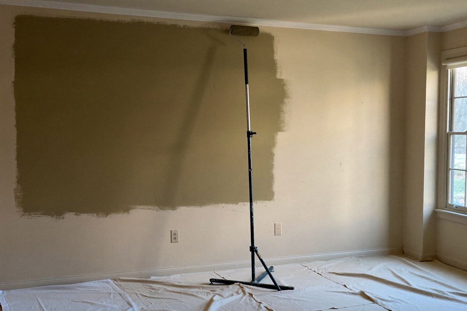 Rolling warm paint onto an interior wall over primer — a paint calculator converts wall area into gallons