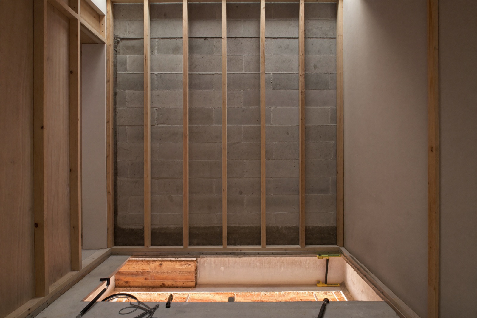 Framing basement walls with wood studs against a concrete foundation — basement finishing cost scales per square foot