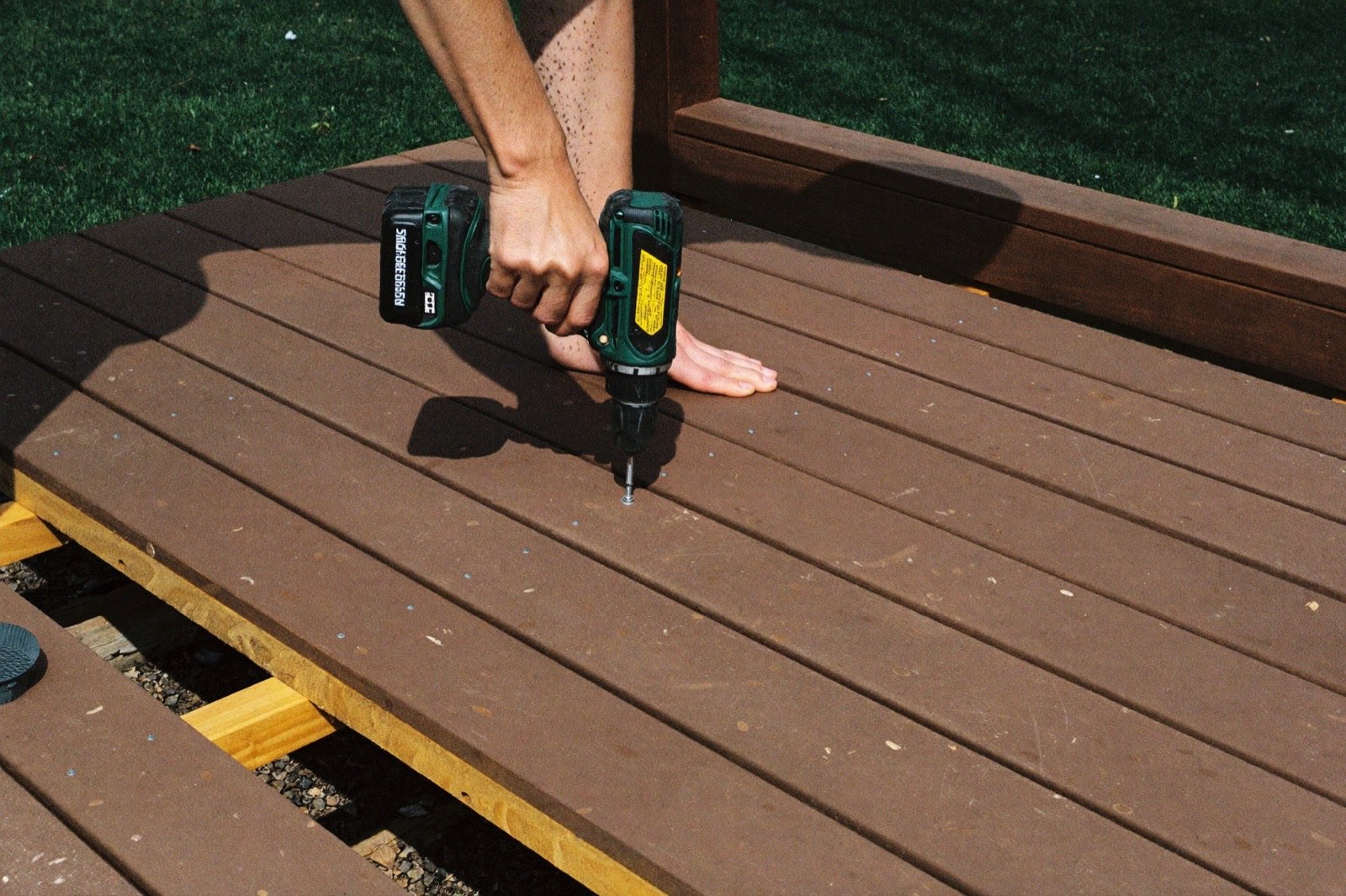 Driving screws into composite deck boards over pressure-treated joists — a deck cost calculator prices framing and decking separately