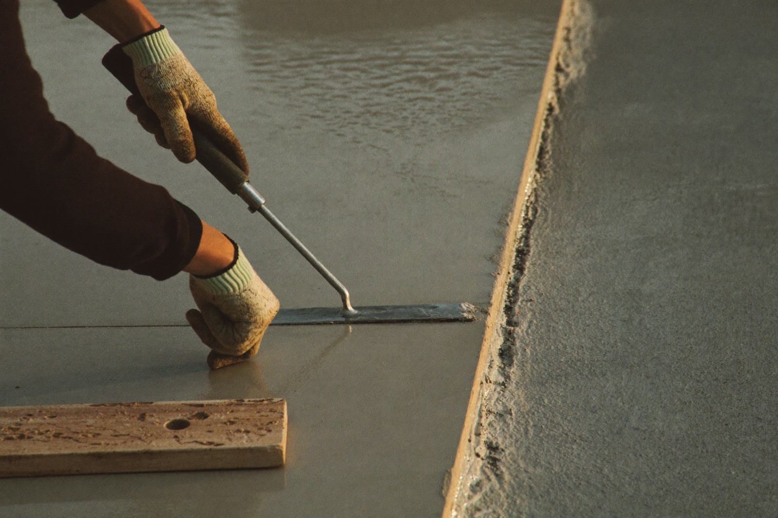 Finishing a concrete slab edge with an edging trowel — finishing labor is part of installed slab cost