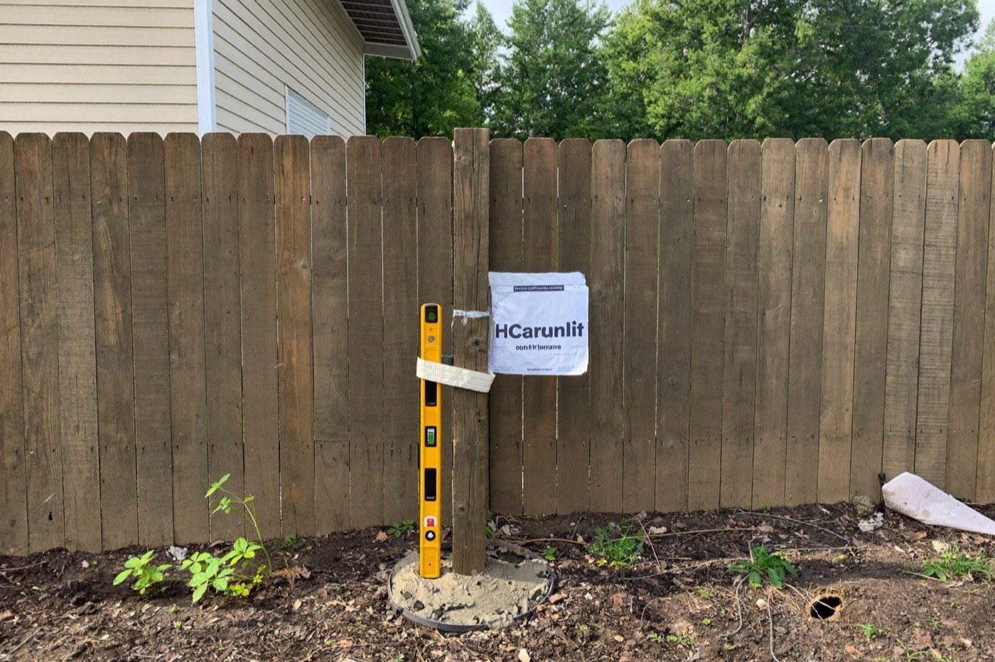 Setting a wooden fence post in fast-setting concrete with a level — a fence calculator counts posts, rails, pickets and bags