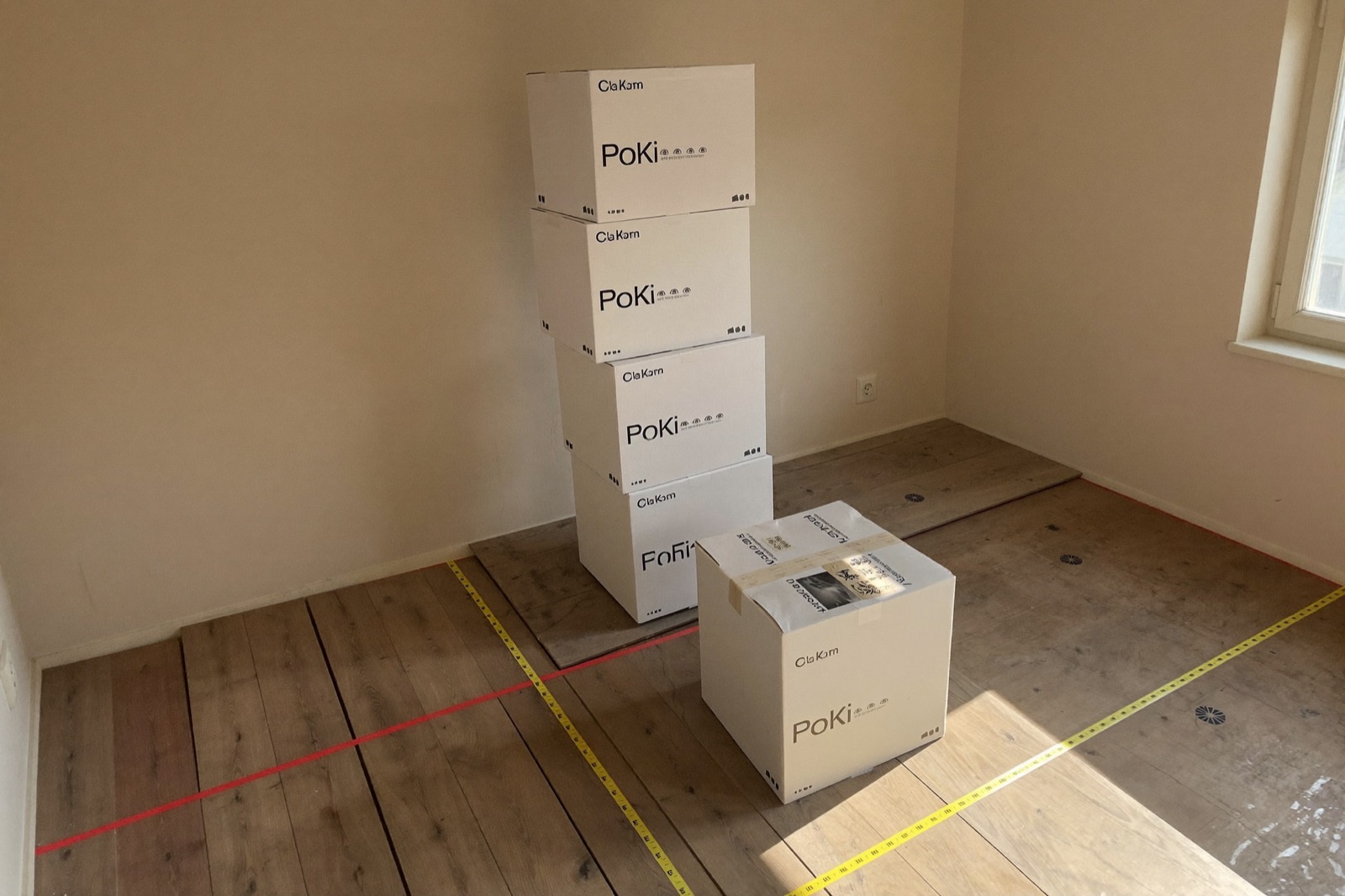 Boxes of plank flooring acclimating in an empty room with spacers — the layout pattern sets the waste factor