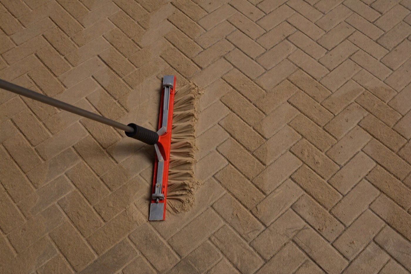 Sweeping polymeric sand into herringbone paver joints — the laying pattern changes the waste factor