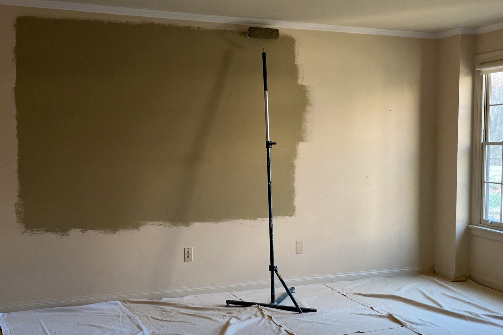 Rolling warm paint onto an interior wall over primer — a paint calculator converts wall area into gallons