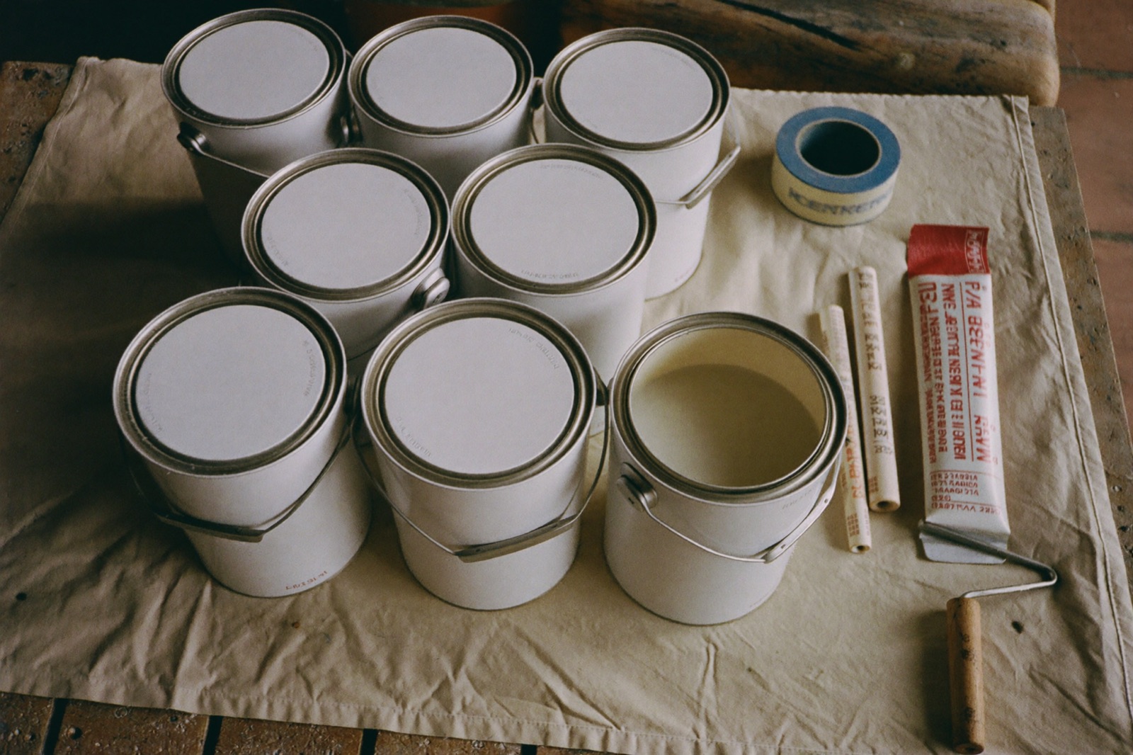 Gallon paint cans, roller tray and painter’s tape on a drop cloth — gallons and primer counted per coat