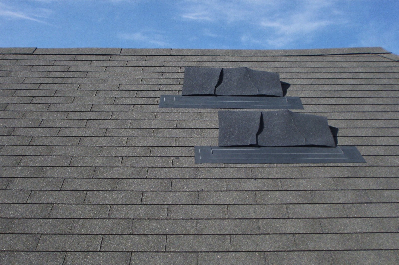 Roofer installing architectural asphalt shingles with bundles staged on the roof — a roofing calculator converts footprint to squares and bundles