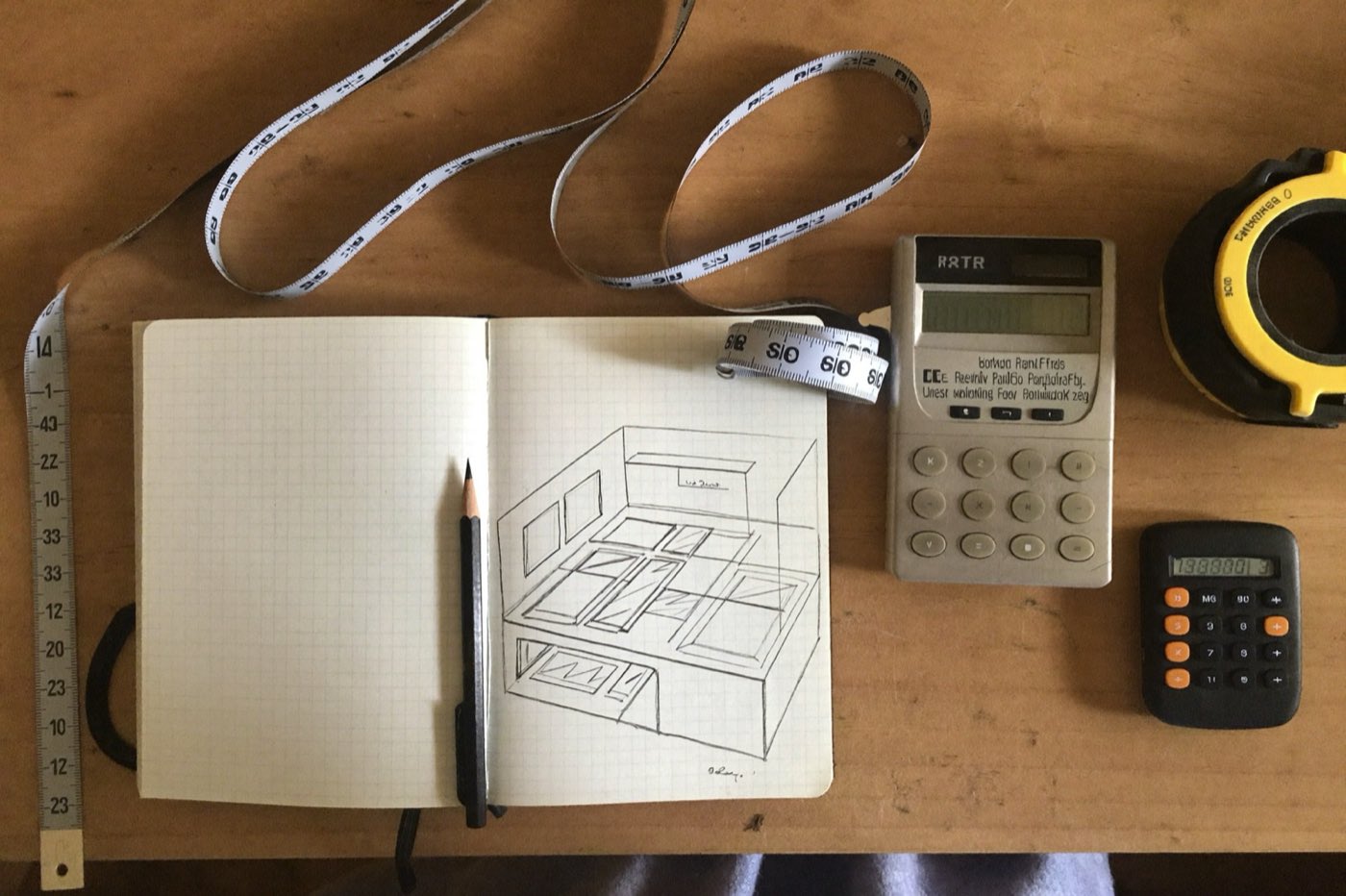 Tape measure, pencil, graph-paper sketch and calculator on a workbench — planning a material takeoff