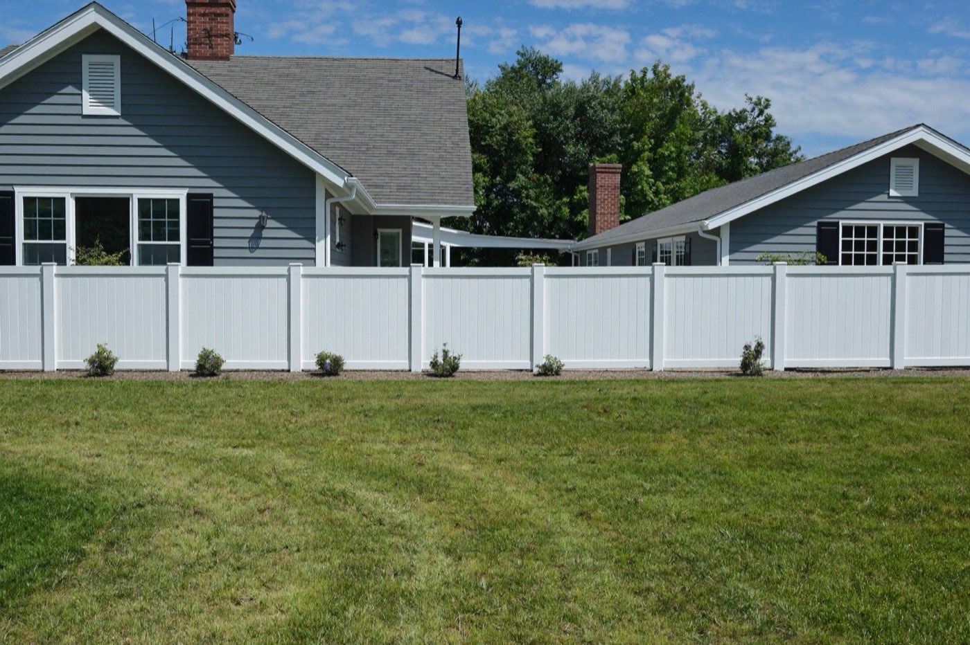 White vinyl fence panels along a front yard — vinyl vs wood vs chain-link installed cost comparison